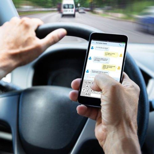 Close-up Of A Man's Hand Typing Text Message On Mobile Phone While Driving Car